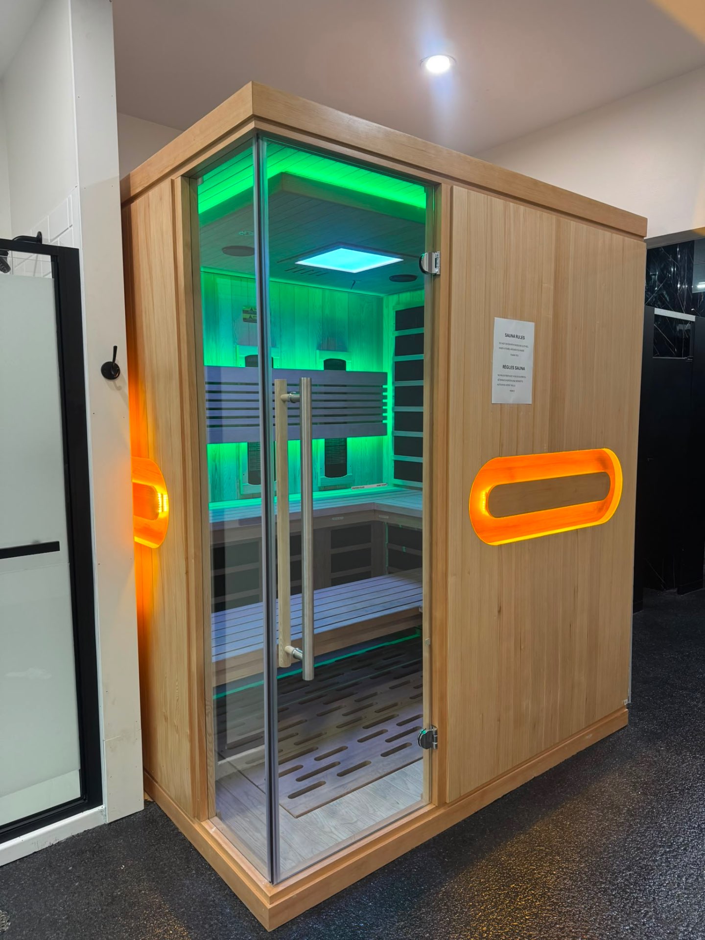 Intérieur du sauna infrarouge du Club Fitness baigné d'une lumière verte de chromothérapie, banc en bois clair et parois vitrées — ambiance calme, LaSalle, Montréal